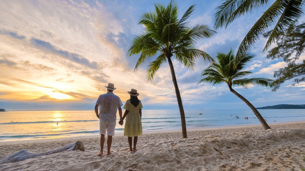 A couple takes in a romantic sunset while holding hands on a beach in Phuket