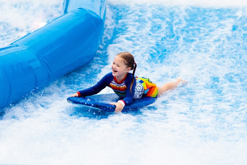 Little girl riding a bodyboard on a wave simulator