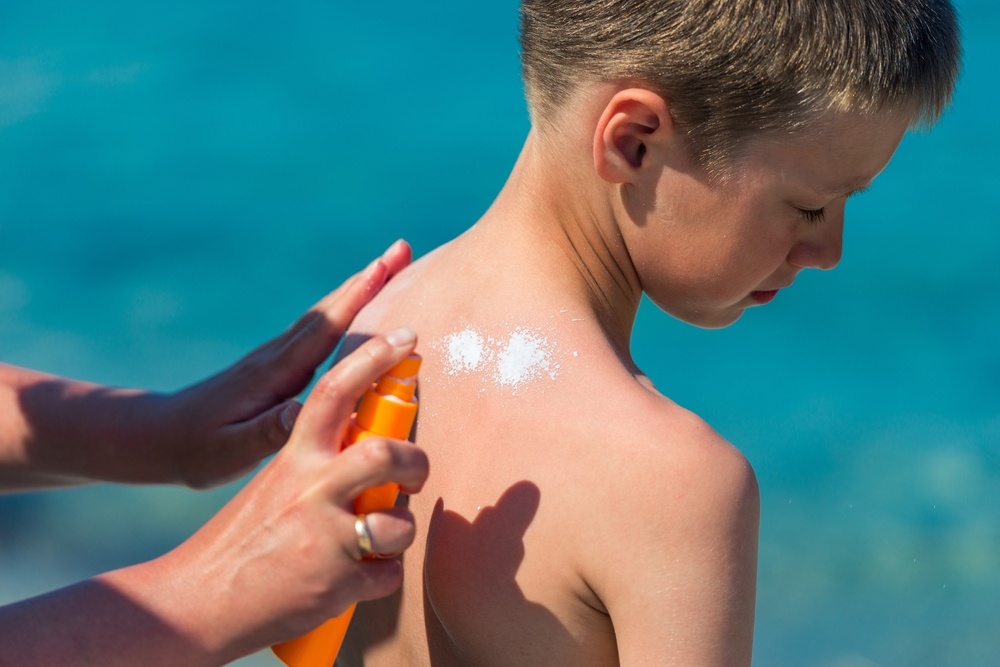 a mother applies sunscreen to the back of her young son